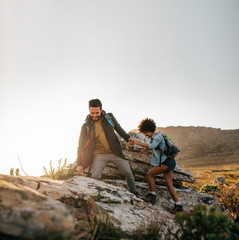 Wall Mural - young couple hiking help each other in mountains