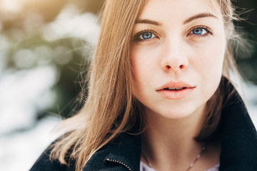 Wall Mural - Closeup portrait beautiful blue eyes girl in black coat walking in winter park