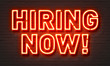 Hiring now neon sign on brick wall background.