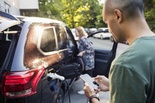 Man Using Smartphone With Woman Standing By Car In Background