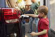© Maskot - Boy plugging charger to electric car