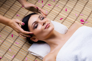 Beautiful, young and healthy woman on bamboo mat in spa salon having temple massage. Spa, health and healing concept.