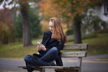 Young Woman Sitting On Bench And Using Mobile Phone