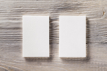 Closeup mockup of two blank vertical business cards at light natural wooden background.