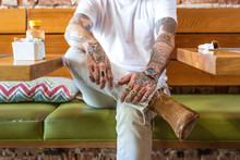Man Sitting In Cafe With Tattooed Arms And Hands, Mid Section 