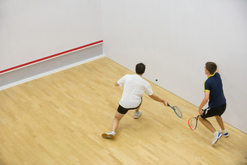 Squash players in action on squash court, back view/Two men playing match of squash.