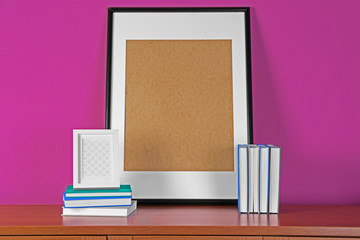 Poster - Books and frame on wooden table against pink background