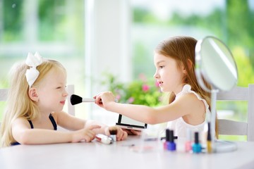 Two cute funny sisters applying make-up on sunny summer day at home