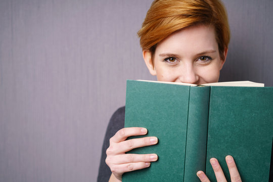 lachende frau versteckt sich hinter einem buch