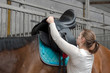 Frau sattelt Pferd mit Sattel aus Leder