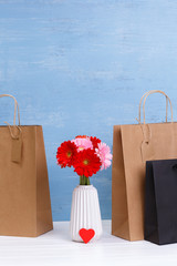 Wall Mural - Mockup of blank shopping bags. Gerbera flowers and red heart. Brown and black craft packages. Concept for sales or discounts. Blue wooden rustic board.