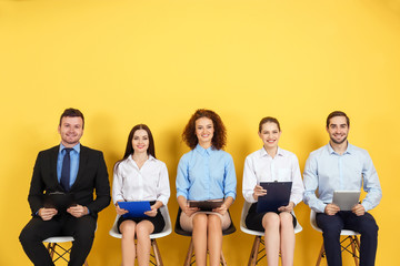 Group of people waiting for job interview on yellow wall background