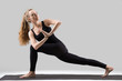 © fizkes - Young attractive yogi woman practicing yoga, standing in Revolved Side Angle exercise, Parivrtta Parsvakonasana pose, working out, wearing sportswear, black tank top, pants, full length, grey studio