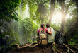 Couple hikers with backpacks enjoying view waterfall in rain forest