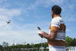 © DragonImages - Middle-aged man standing in sunny park against blue sky and operating drone with the help of remote controller
