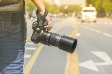 Photographer holding a camera standing on the street in the morning light with blur background  and bokeh.