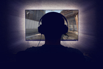 Gamer in headphones sits in front of a blank monitor in dark room