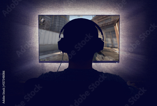Gamer in headphones sits in front of a blank monitor in dark room Wallpaper Mural