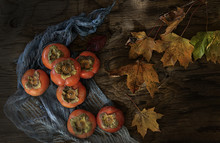 Overhead View Of Persimmons And Autumn Leaves On Wooden Table