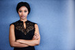 © nakophotography - Attractive young adult black woman looking into camera with her arms crossed and a serious facial expression with a blue textured background behind her.