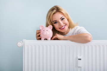 Happy Woman With Piggybank On Radiator