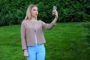 Wall Mural - Young cute girl holding phone at arm's length and directs smiles