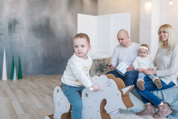 Wall Mural - Baby boy on wooden horse swing. Parents with the little sister on background.