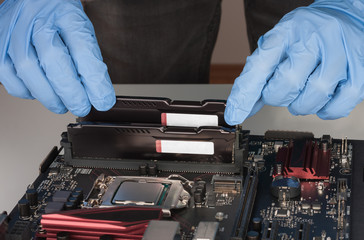 Close up of man hands with gloves installing Ram DDR4 memory module in slot on motherboard