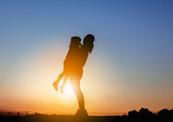 Silhouettes of mother and daughter playing at sunset evening sky background.