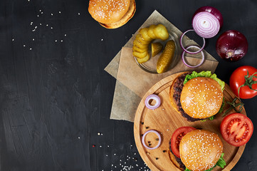 Wall Mural - Craft beef burgers on round wooden cutting board with vegetables. Flat lay on black textured background.