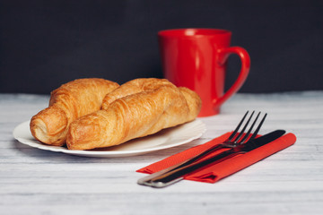 two croissants on a saucer cutlery Red mug