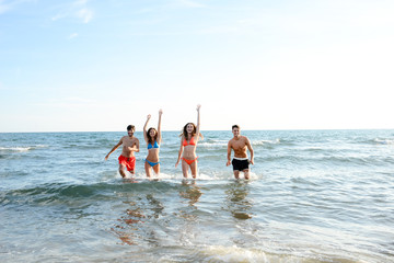 Wall Mural - four happy friends young people man and woman having fun at ocean beach jumping together in the sea