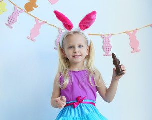 Wall Mural - Cute little girl with bunny ears and chocolate rabbit at home