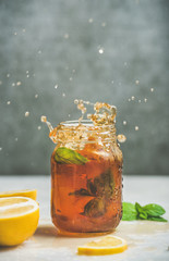 Wall Mural - Summer cold Iced tea with fresh bergamot, mint and lemon in glass jar with splashes, grey concrete wall at background, copy space. Food in motion concept