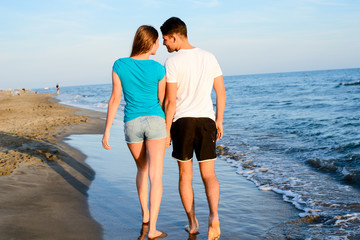 romantic young couple walking barefoot together in sand along the beach of mediterranean sea at sunset