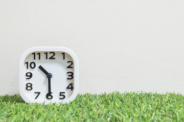 Closeup white clock for decorate show a half past ten, or 10:30 a.m. on green artificial grass floor and cream wallpaper textured background with copy space