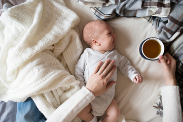 Unrecognizable mother with newborn baby son lying on bed