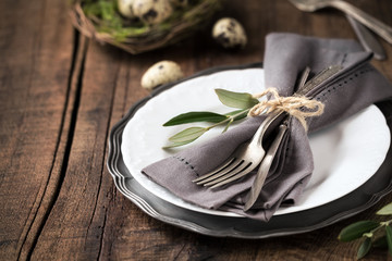 Easter table setting with vintage silverware with an olive branch on a white plate with quail eggs in a decorative nest at the background. With copy space for your text