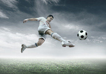 Wall Mural - Football player with ball in action under sky with clouds