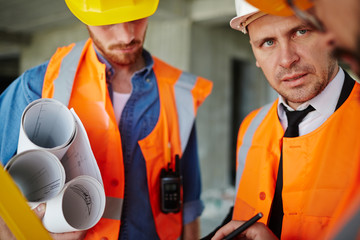 Portrait of foreman inspector talking to two workmen wearing protective vests and hard hats