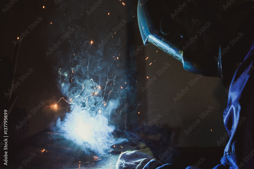 Industrial workshop man welding round pipe on a metal work table, colorful smoke, sparks and reflections - obrazy, fototapety, plakaty 