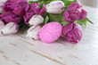 Rosa Osterei vor weißen und pinken Tulpen auf Holzuntergrund an Ostern