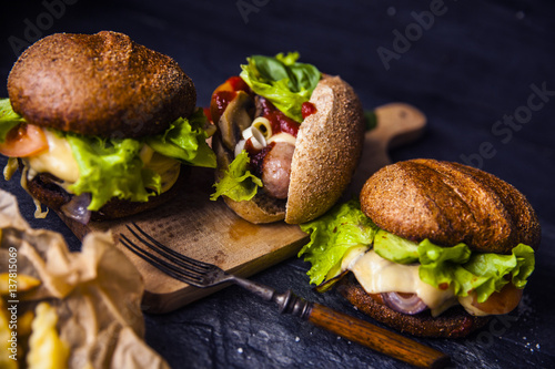 Fast food on the table: hot dog sausage and vegetables, burger with pork or beef and French fries with tomato sauce, basil leaves © lebedevaelena