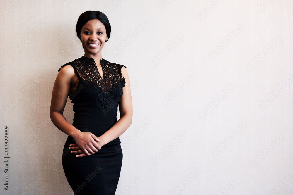 classy black woman smiling into the camera while posing in a beautiful black dress against a textured beige wall, with excitement visible in her facial expression. Stock Photo | Adobe Stock classy black woman smiling into the camera while posing in a beautiful black dress against a textured beige wall, with excitement visible in her facial expression. Stock Photo | Adobe Stock