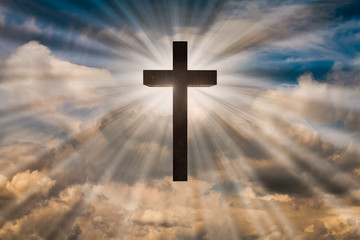jesus christ cross on a sky with dramatic clouds and bright sun rays, sunbeams behind the wooden cro