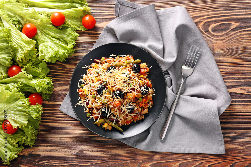 Tasty rice with vegetables in black plate on table