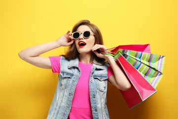 Wall Mural - Beautiful young woman with paper bags on color background