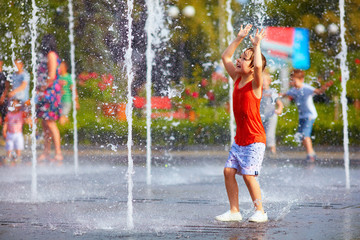 Wall Mural - excited boy having fun between water jets, in fountain. Summer in the city