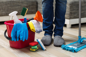 Wall Mural - Cleaning service. Bucket with sponges, chemicals bottles and mopping stick. Rubber gloves, plunger and towel. Man standing in slippers.