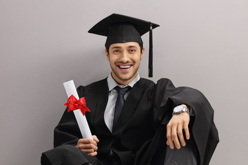 Happy graduate student with diploma leaning against gray wall